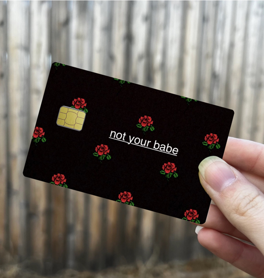 Credit card skin with black background, red pixel rose pattern, and white text that reads "not your babe", chip cutout on the left
