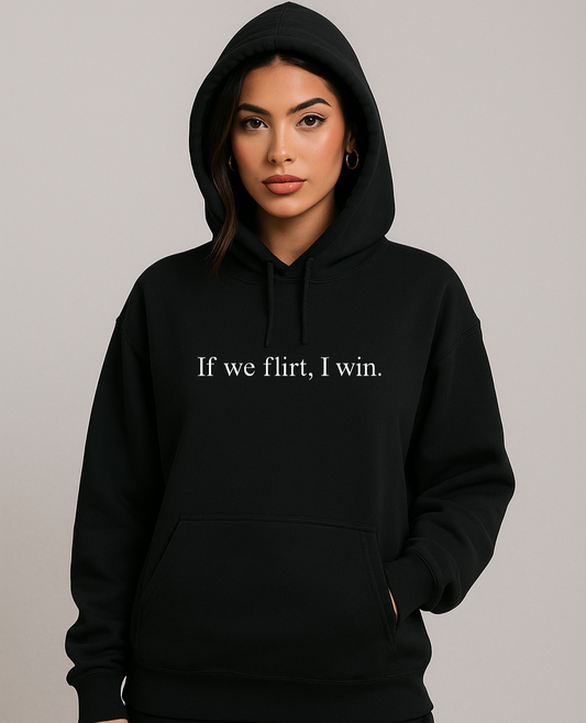 Young woman wearing black hoodie with white text that reads "If we flirt, I win." Styled with gold hoops and soft glam makeup, posed confidently in streetwear aesthetic.