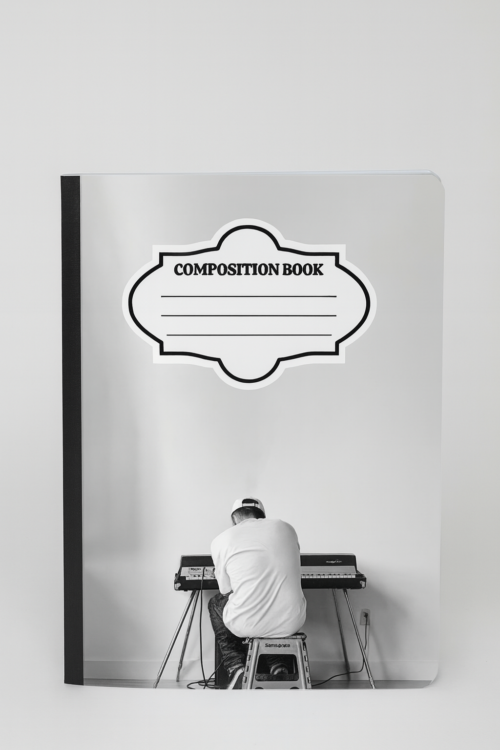 Black and white composition notebook with a minimalist photo of a man sitting at a keyboard against a blank wall, Mac Miller aesthetic